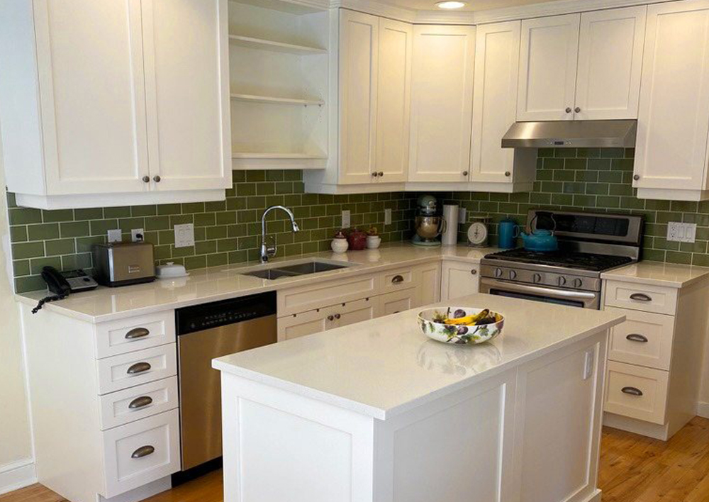 A refaced Nanaimo kitchen with white shaker doors run up to crown moulding, an olive-green subway backsplash, quartz counters and a panelled island