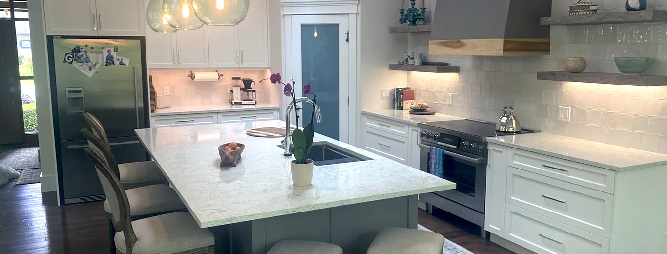 A full custom Nanaimo kitchen with white shaker cabinetry, a large quartz island with seating, glass pendant lights, a plaster range hood and floating wood shelves under a skylight