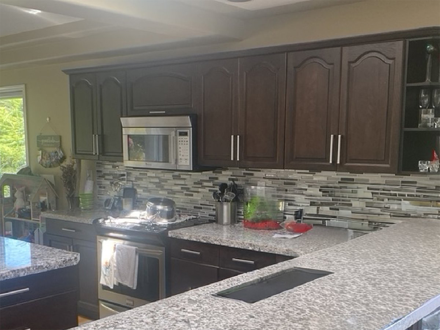 The Bender kitchen in Nanaimo before its partial renovation, with dark espresso raised-panel doors, a busy grey granite counter and a glass-tile backsplash