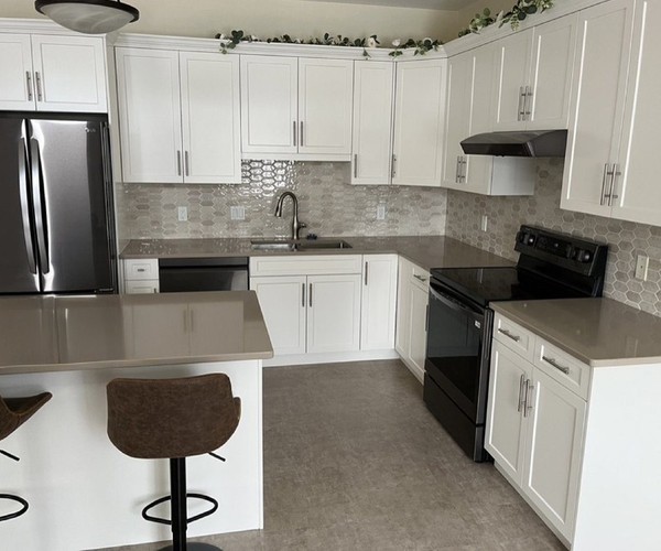 A refaced Nanaimo kitchen with white shaker doors, stone counters and a breakfast bar