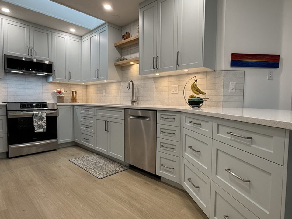 A pale grey shaker kitchen with a skylight, open wood shelving and a tile backsplash