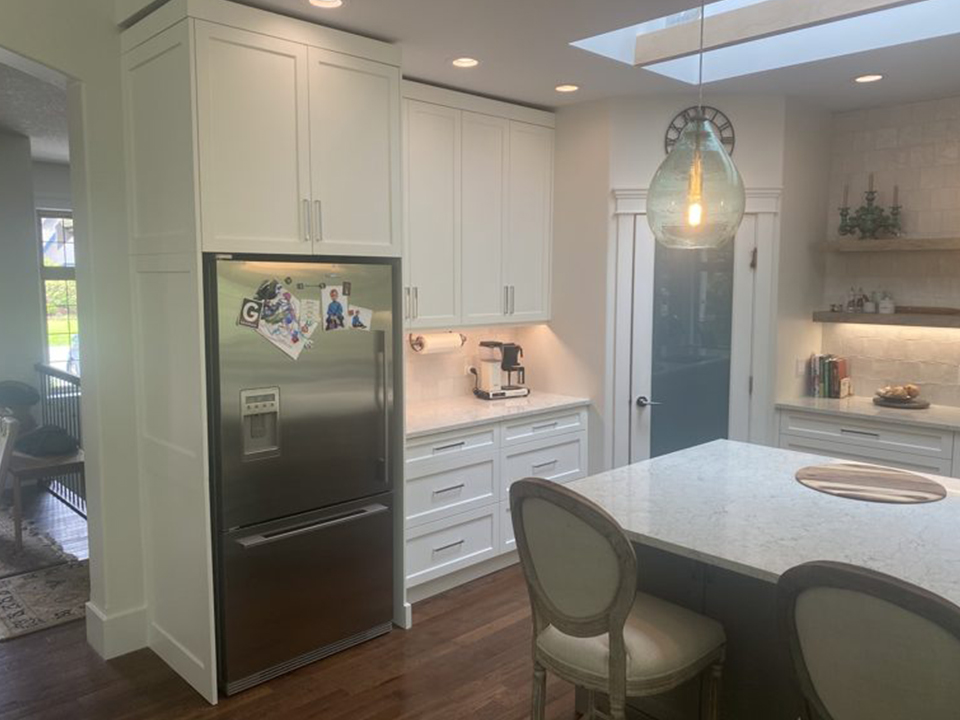 A full custom kitchen with white shaker cabinets, a quartz island with seating and a skylight overhead
