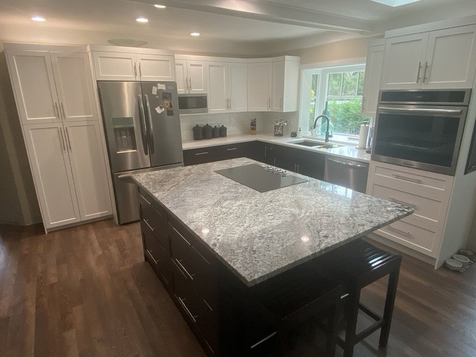 A two-tone kitchen with white shaker uppers and tall pantry cabinets above dark espresso lowers and a granite-topped island