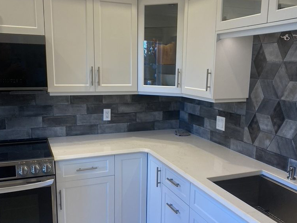 A white shaker kitchen with quartz counters and a slate-toned geometric tile backsplash
