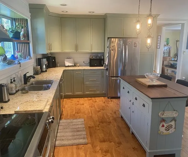A sage-green kitchen with granite counters and a freestanding island with a wood top