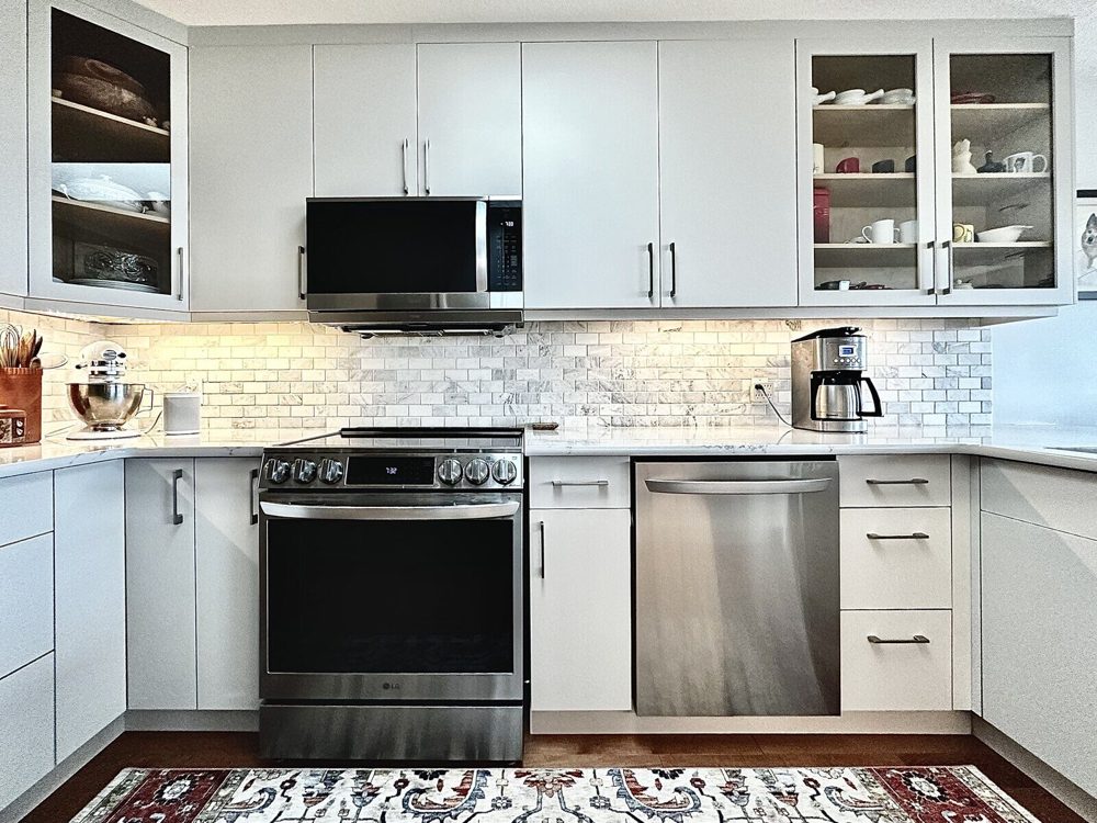 The same kitchen after its partial renovation, with light grey flat-panel doors, new uppers taken to the ceiling and glass-insert display doors