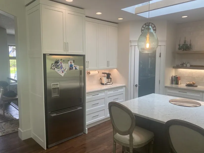 A full custom kitchen with white shaker cabinets, a quartz island with seating and a skylight overhead