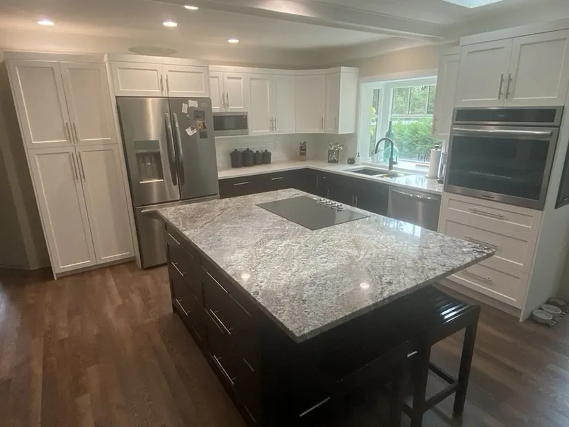 A two-tone kitchen with white shaker uppers and tall pantry cabinets above dark espresso lowers and a granite-topped island