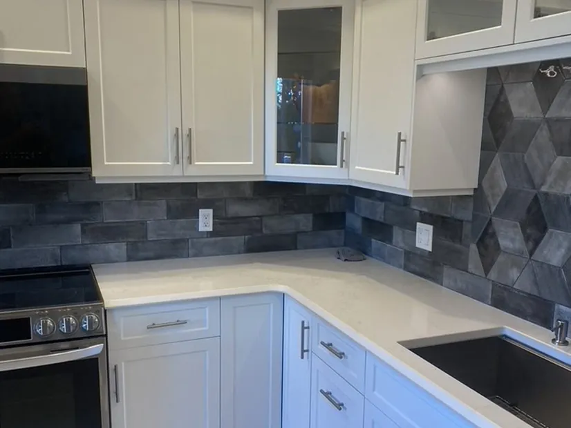 A white shaker kitchen with quartz counters and a slate-toned geometric tile backsplash