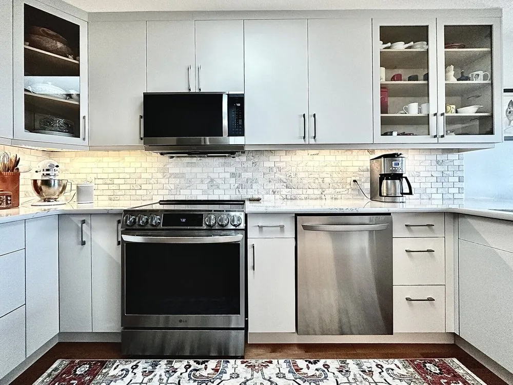 The same kitchen after its partial renovation, with light grey flat-panel doors, new uppers taken to the ceiling and glass-insert display doors